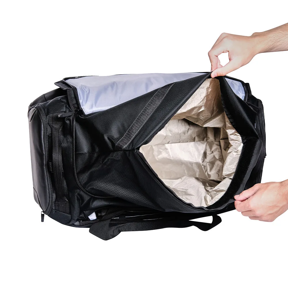 Deux mains ouvrent le compartiment principal blindé du sac Faraday Duffel, la doublure apparente