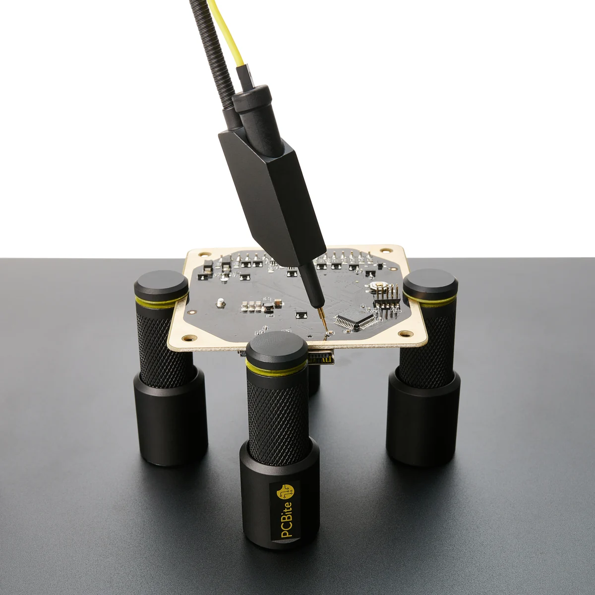 Une carte électronique tenue par quatre supports PCBite, une sonde posée sur un composant